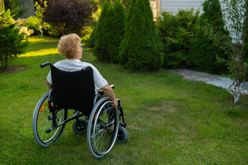 Peaceful elderly woman sitting in a wheelchair on a walk outdoors. 