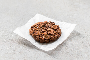 Vegan Chocolate cookie with oatmeal, chocolate chips and hazelnuts. On paper. Light grey background. Close up
