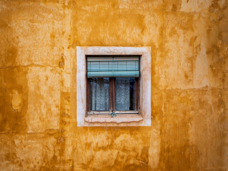 Detail of a yellow building facade, square homey window with green shutter and curtains from the old town of the unesco world heritage city of Cuenca, Spain