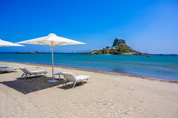 Deck chair and umbrella on beautiful Agios Stefanos Beach in front of paradise Island Kastri- historical ruins and paradise scenery at coast of island Kos, Greece