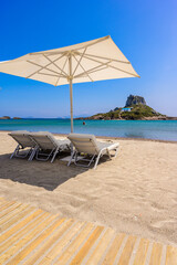 Deck chair and umbrella on beautiful Agios Stefanos Beach in front of paradise Island Kastri-...