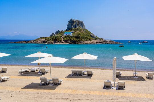 Deck chair and umbrella on beautiful Agios Stefanos Beach in front of paradise Island Kastri- historical ruins and paradise scenery at coast of island Kos, Greece