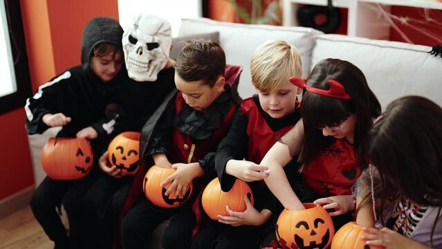 Group of kids wearing halloween costume putting candies in pumpkin basket at home
