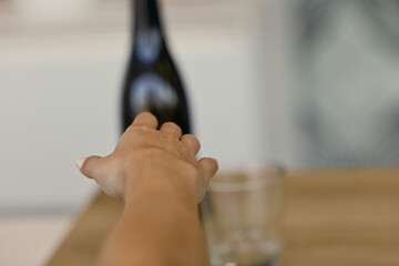 Hand reaches for bottle, trying to forget sorrow