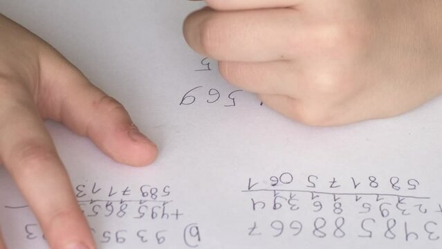 child, schoolchild hesitantly solves difficult task of adding numbers, writes down numbers, makes mistakes in notebook with pen, math lessons, education concept, elementary school