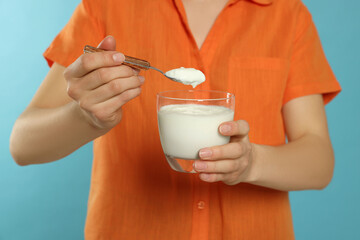 Closeup of woman with tasty yogurt on light blue background