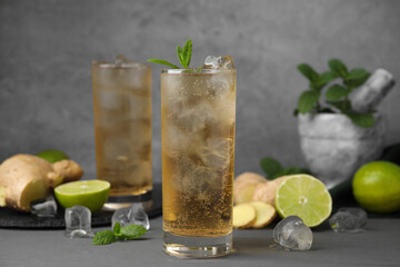 Glass of tasty ginger ale with ice cubes and ingredients on grey table
