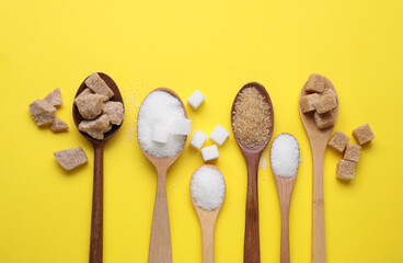 Spoons with different types of sugar on yellow background, flat lay