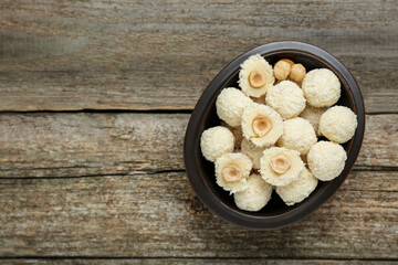 Delicious candies with coconut flakes and hazelnut on wooden table, top view. Space for text