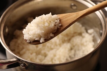 Wooden spoon with delicious rice over pot, closeup
