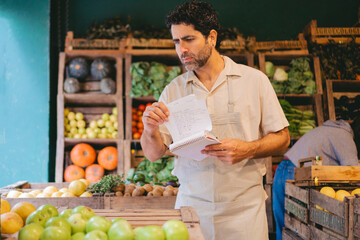 Latin middle-aged man greengrocer taking inventory in a notebook in his organic greengrocer's shop. copy space