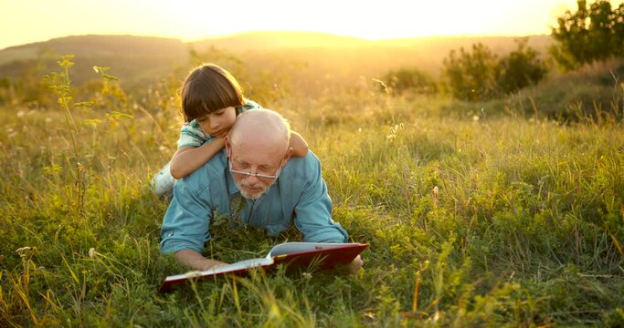 Granfather and grandson laying in grass and reading a book