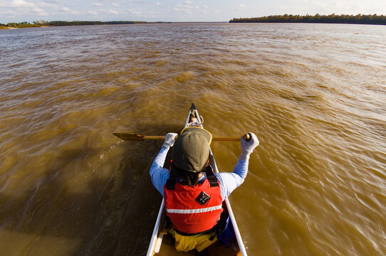 Overhead shot of a woman in a red life preserver paddling paddles a canoe the Mississippi River
