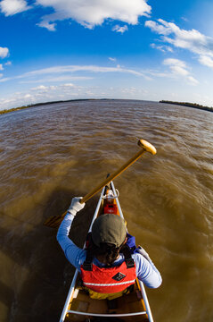Overhead fisheye shot of a woman in a red life preserver paddling paddles a canoe the Mississippi River