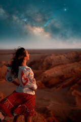woman standing on a lookout over a desert valley with stars and milky way on the horizon