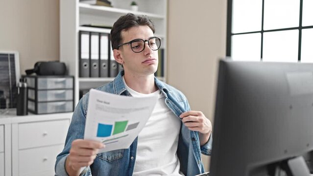 Young hispanic man business worker using documents as a hand fan at office