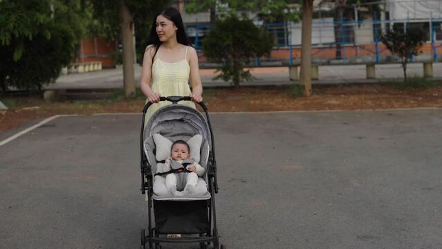 happy mother pushing infant baby stroller and walking in the park