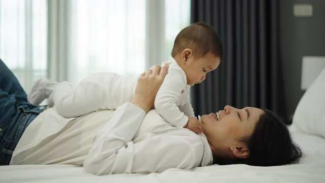 happy mother lying and playing with her infant baby on a bed