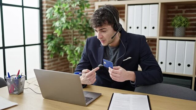 Young hispanic man business worker wearing headset on a video call using credit card at office