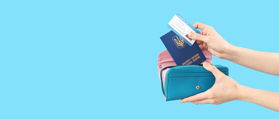 Woman putting Ukrainian passport and vaccination card in wallet on blue background with space for text