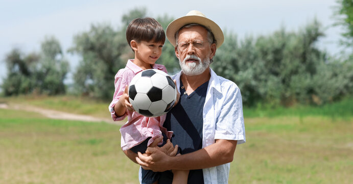 Little boy with ball for playing football and his grandfather in park