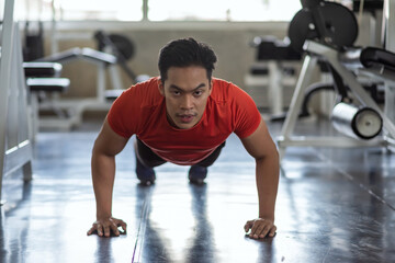Fototapeta na wymiar Muscular Asian young athlete man pushs up training on floor at gym