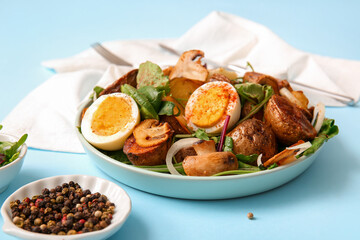 Plate of tasty potato salad with eggs and mushrooms on light blue background