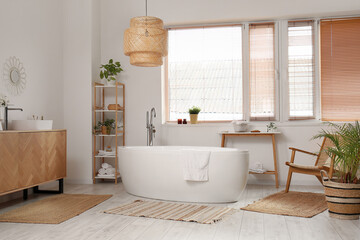 Interior of bathroom with bathtub, wooden cabinet and shelving unit near window