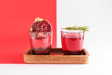 Board with glasses of fresh pomegranate juice on colorful background