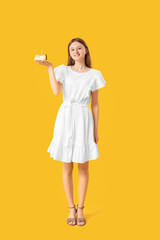Pretty young woman with birthday cake on yellow background