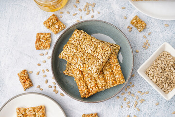 Plates with tasty kozinaki, sunflower seeds and jar of honey on white grunge background