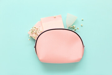 Lady's cosmetic bag with menstrual cup and pads on turquoise background