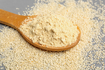 Wooden spoon with sesame flour and seeds on grunge grey background