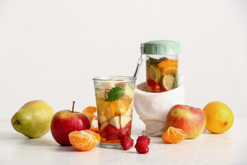 Glass and sports bottle of infused water with different sliced fruits on white table