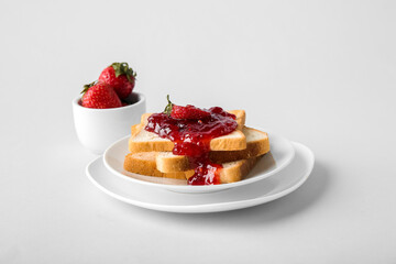 Plates and tasty toasts with strawberry jam on white background
