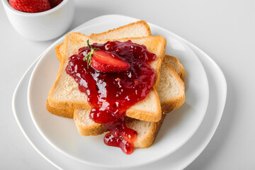 Plates and tasty toasts with strawberry jam on white background