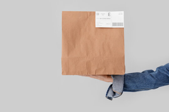 Female hand holding paper bag on grey background. Food delivery