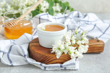 Bowl of honey with flowers of acacia on light background, closeup