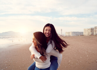 Latin mother with her daughter on a happy piggyback ride on the beach having a good time