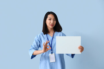 Female Asian medical intern with blank paper sheet on blue background
