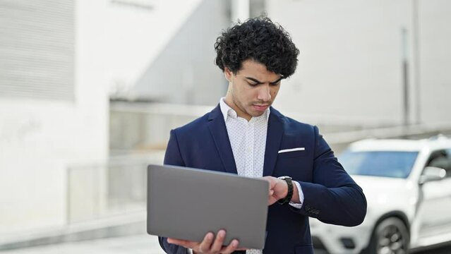 Young latin man business worker looking watch closing laptop at street
