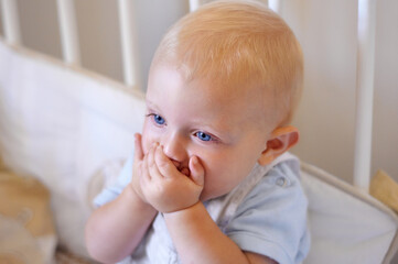 Happy, face and toddler standing in crib, bedroom or excited baby boy with hands on teething mouth for morning surprise of mistake. Kid sitting in cot, awake and healthy bed routine for young child