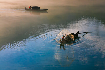 Fishermen netting in early foggy morning with dramatic sunrise background