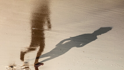 feet of boy running along the beach in the water with shadow and reflection in water
