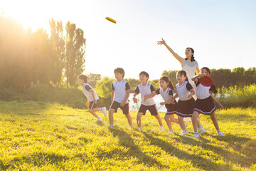 Cheerful school children playing frisbees with their teacher in park