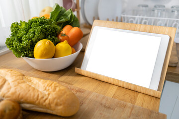 Tablet white screen on kitchen table with Vegetables, fruits and bread. Clipping path. Mockup display empty space use for graphic advertising text. Display live food online media.