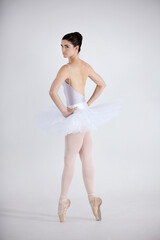 Naklejka premium Portrait, dance and ballet with a woman in studio on a white background for theatre performance rehearsal or recital. Art, creative and back with a young ballerina or dancer standing hands on hips