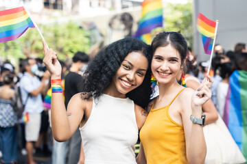 Couple lesbian holding LGBT banner at city street. They looking to camera with attractive smiling.