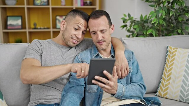 Two men couple hugging each other using touchpad at home