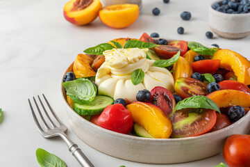 Summer salad with burrata cheese, grilled peaches, tomatoes, blueberries, cucumber, olive oil and basil in a plate